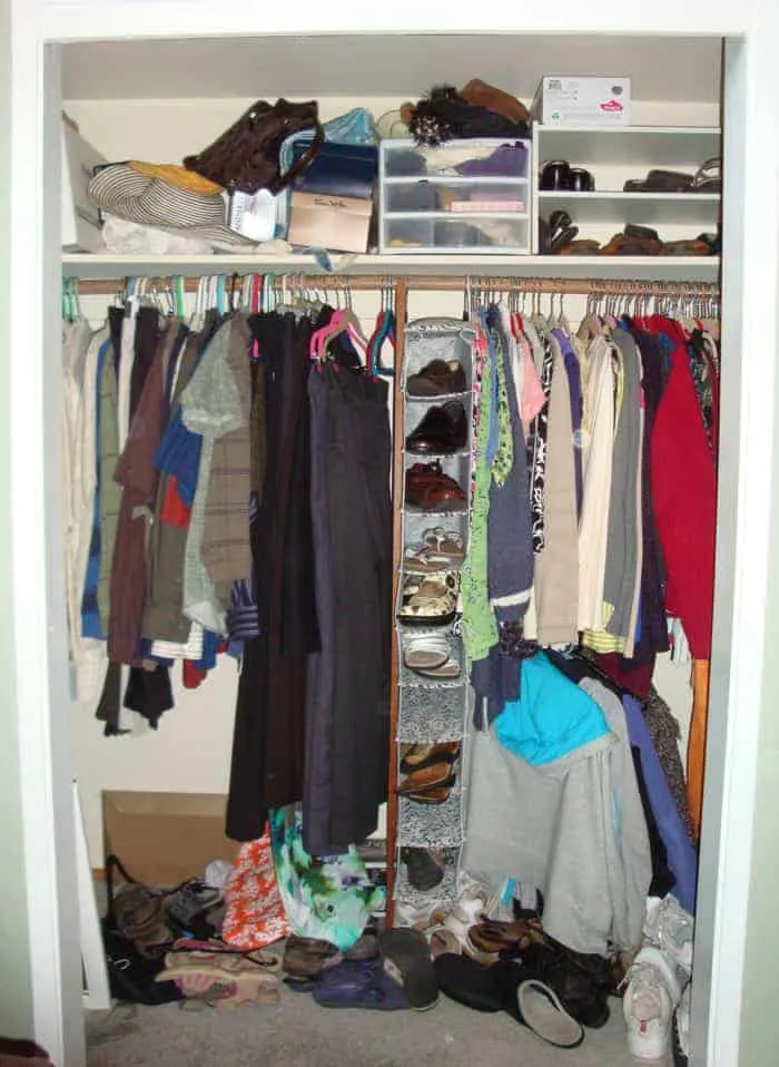Before picture of bedroom closet with no doors and clothes disorganized with shoes in a heap on floor.