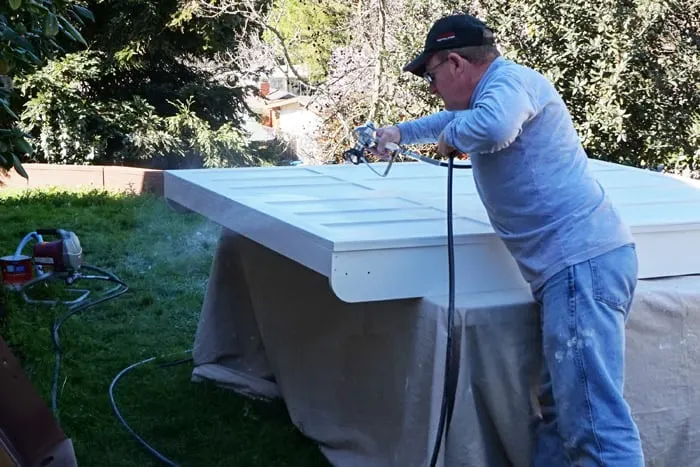 Man using sprayer to paint wood wall bed cabinet front