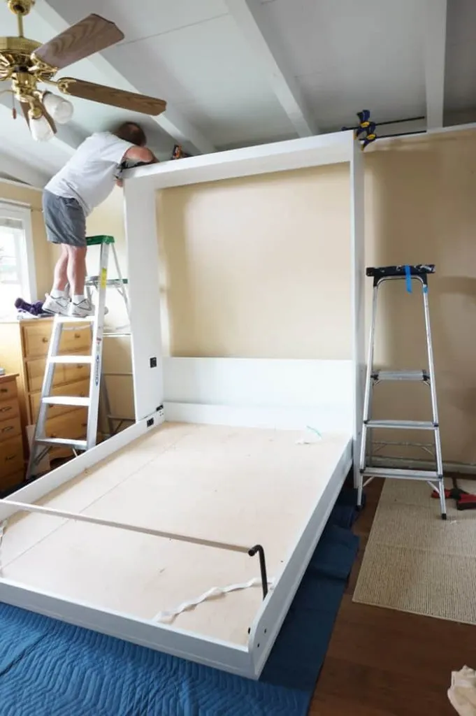 Man on ladder clamping murphy bed header to sides.