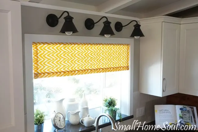 Goose neck lights over kitchen sink above yellow curtains.