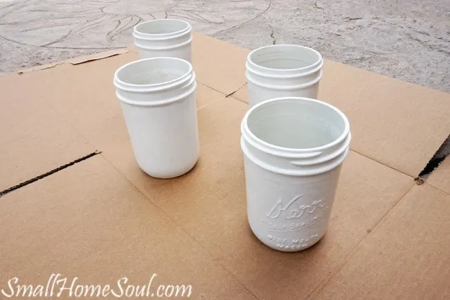 Jars with white paint dry as the rest of the mason jar utensil caddy is created.