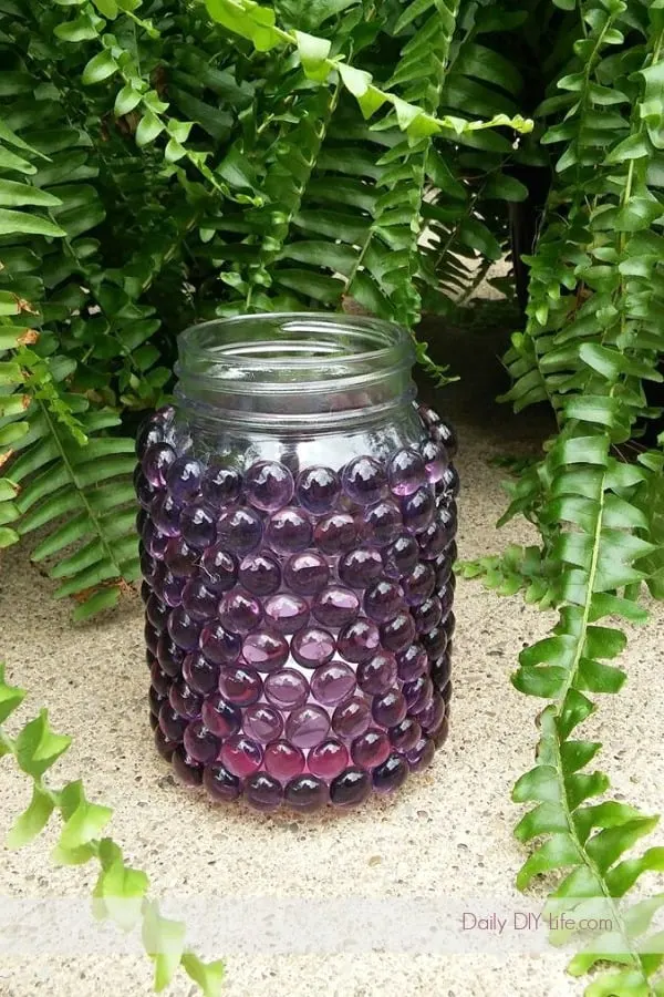 mason jar covered with purple glass beads in front of fern.