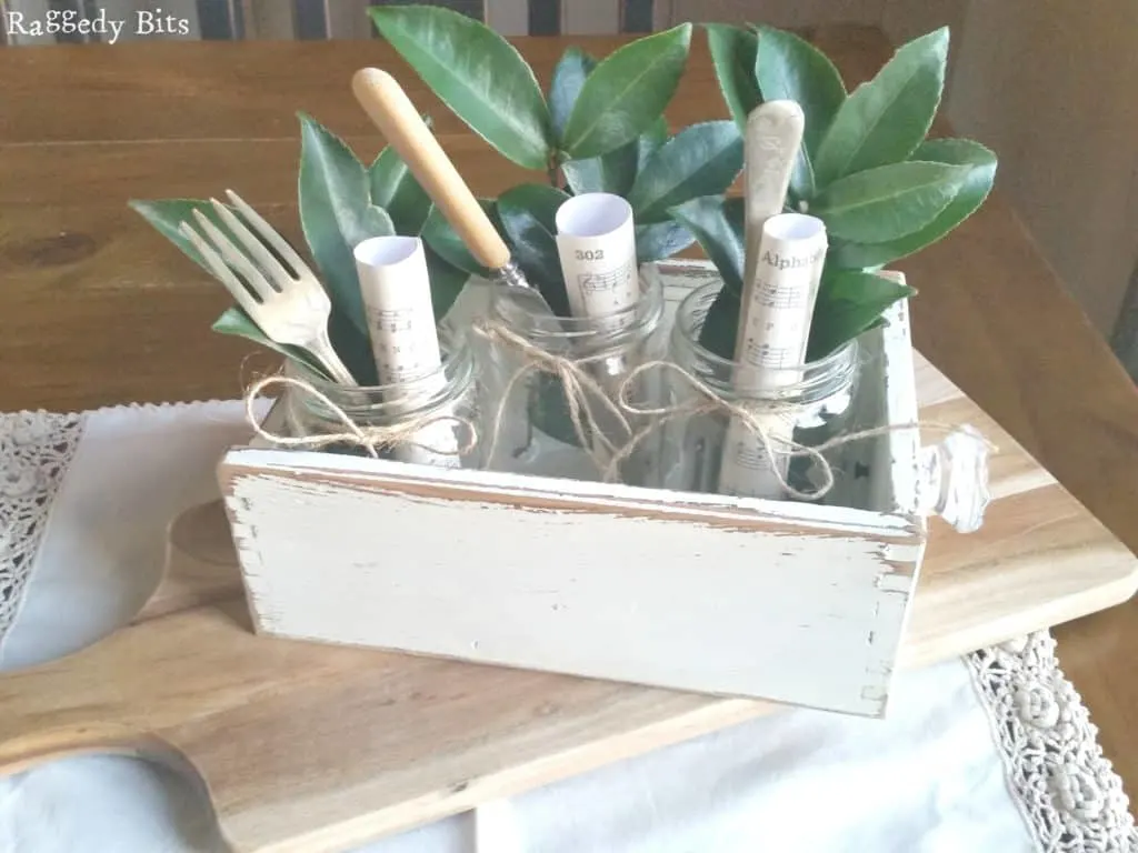 mason jars in wood box filled with single-serve utensils and rolled music notes.