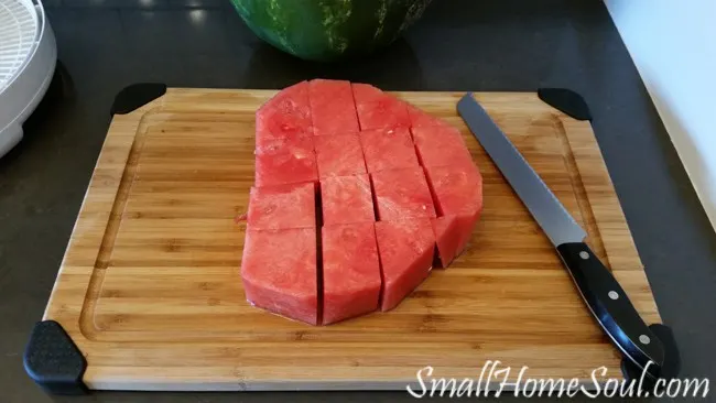 thick slice of watermelon cut into cubes on cutting board.