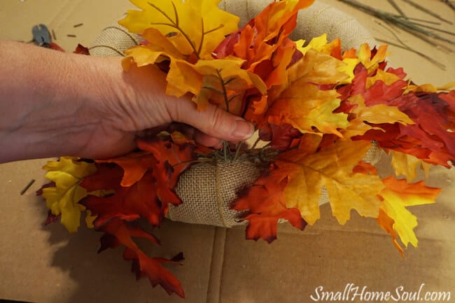 hand pushing maple leaf stems into wreath form.