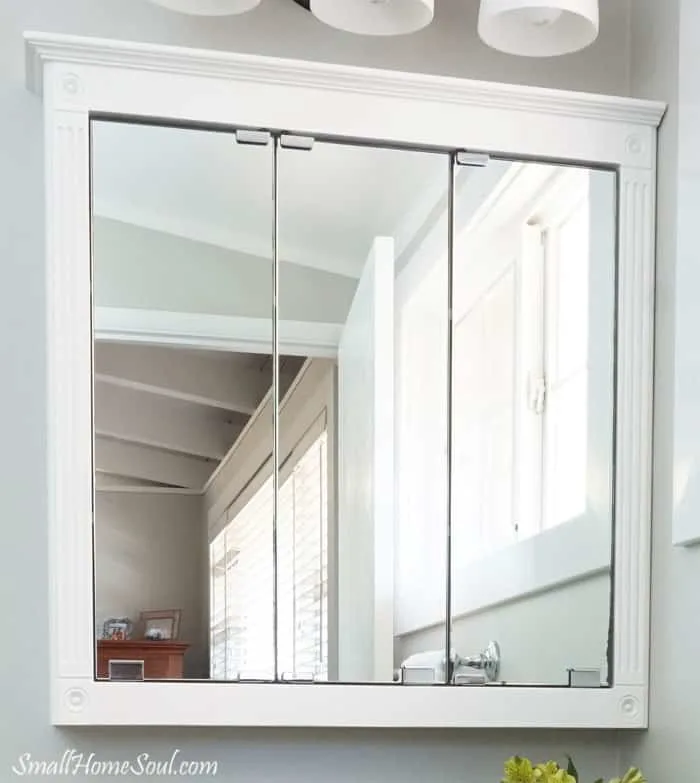 Freshly painted white medicine cabinet above bathroom sink with Door and window in mirror reflection.