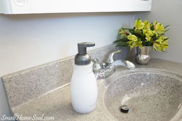 Foaming soap dispenser with newly painted silver top on vanity with yellow flowers in vase