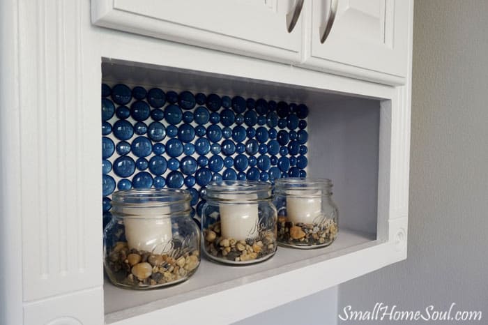 Toilet paper cabinet with blue painted glass wafers on back and candles in foreground.