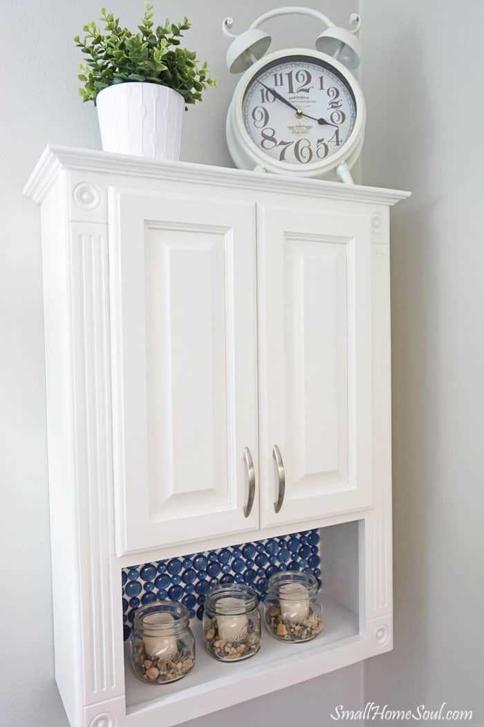 Full view of Toilet Paper cabinet with a clock and green plant on top.