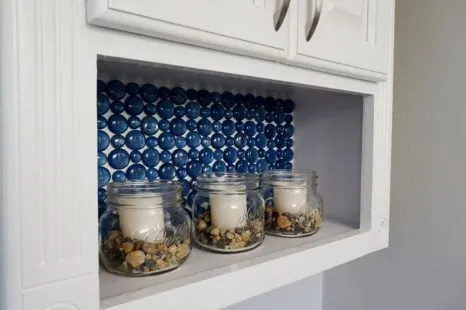 Blue glass backsplash in TP cabinet with candles in jars.