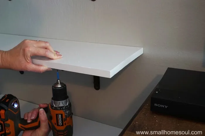 Screwing shelf board to shelf bracket with cordless drill while hand holds steady