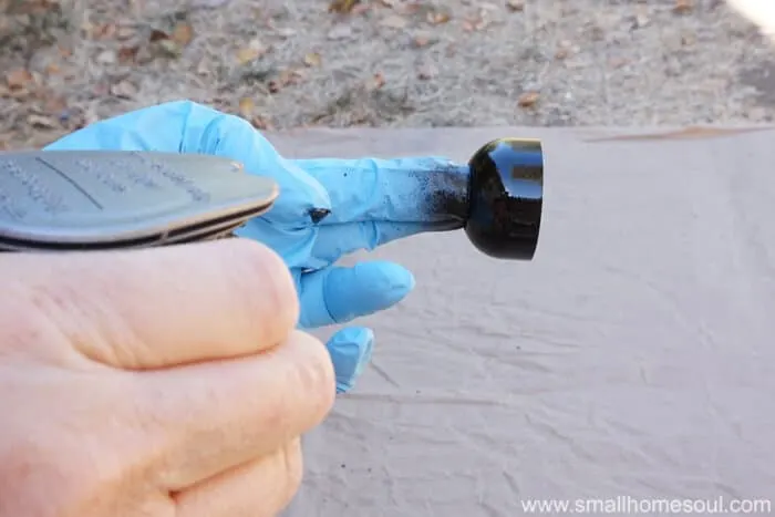 gloved finger holding cap of soap dispenser being painted black.