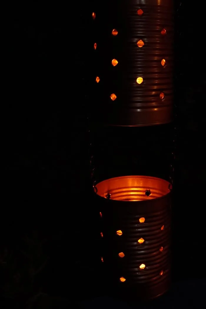 Tin can lights hung and glowing at nigh with a candle.