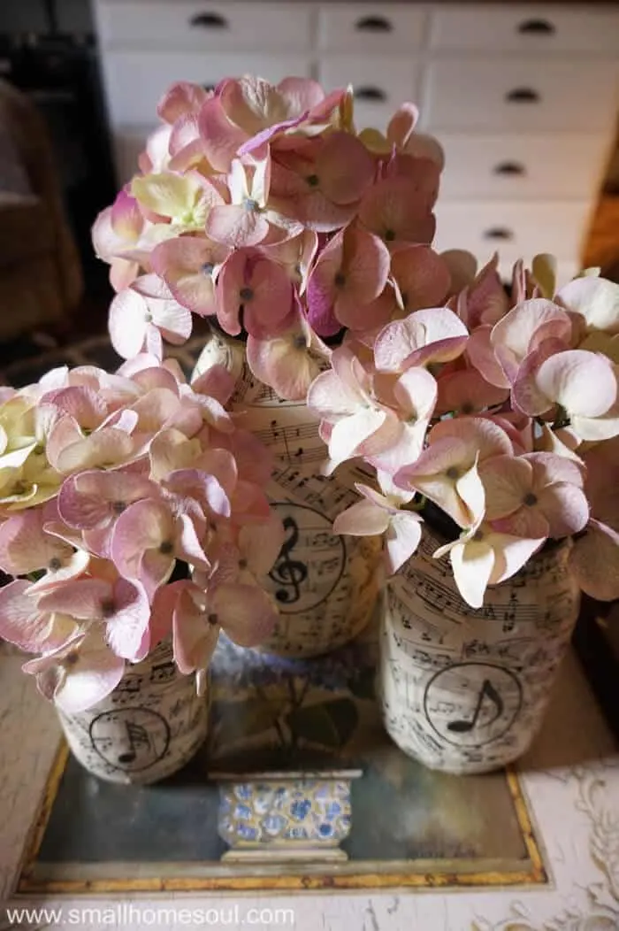 Sheet music mason jar vases filled with faux hydrangeas on coffee table.