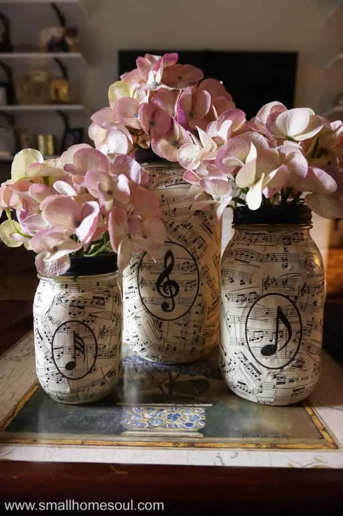 Music sheet mason jar vases filled with colorful hydrangea flowers in tray on coffee table.