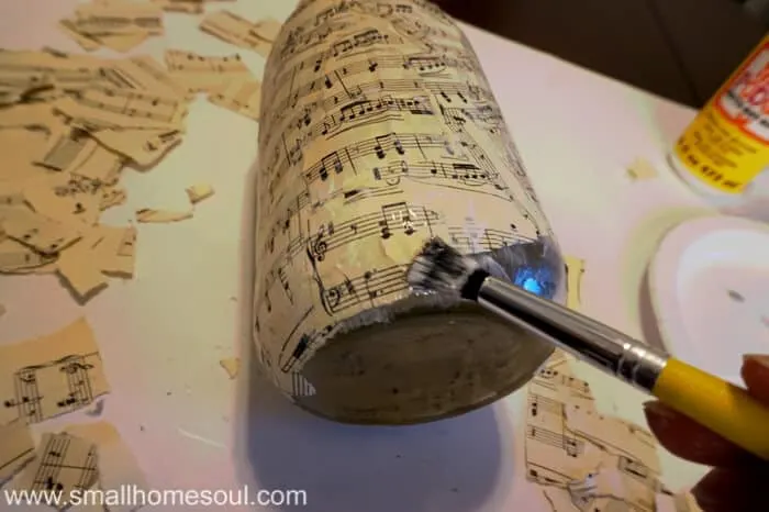 Paintbrush with decoupage gluing on torn sheet music to mason jar.