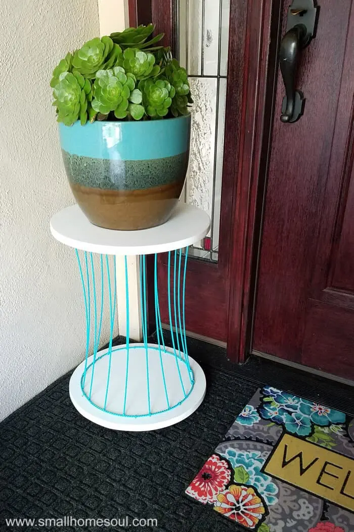 Newly finished outdoor plant stand on porch with a potted plant by front door.