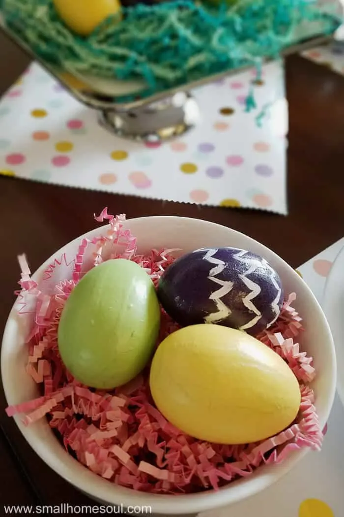 Easter table decorations with colorful eggs in a bowl with pink paper grass.