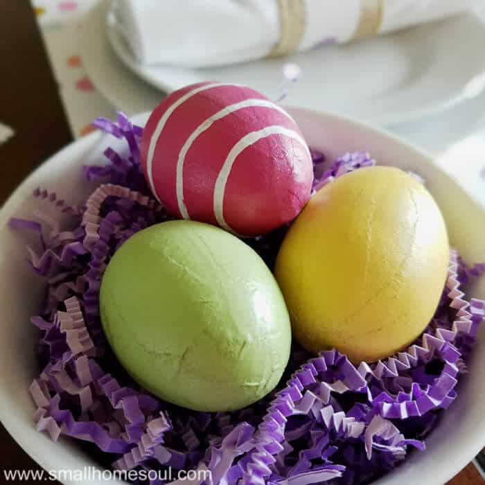 Easter table decorations with colorful eggs in a bowl with purple paper grass.