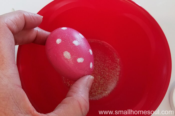 Pink painted egg being held with glue and clear glitter dots.