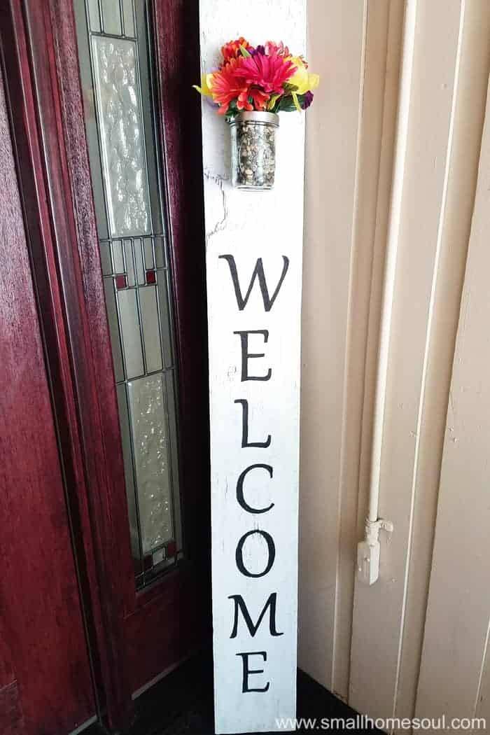 DIY sign propped in corner of porch by front door with flower vase at top