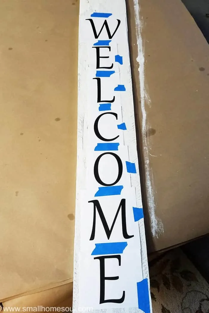 All letters for word welcome taped together onto painted fence board.