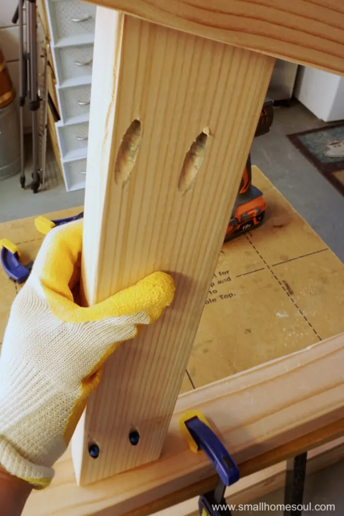 gloved hand holding Table leg assembly for screwing.