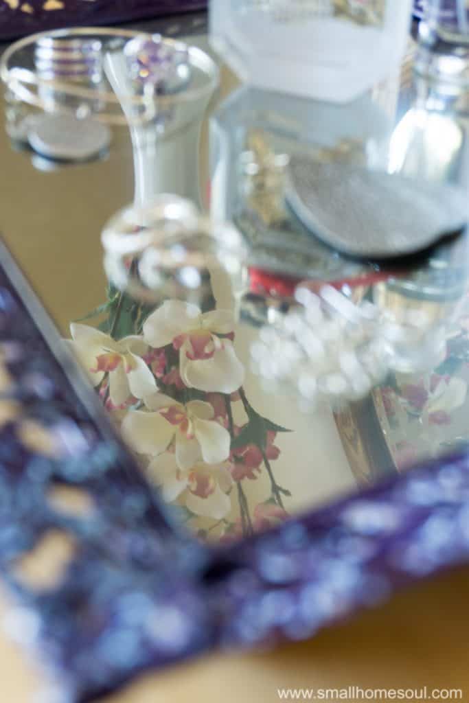 Mirrored finish on the jewelry tray reflects flower from a vase.