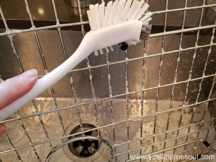 Scrubbing the sink grid with a scrub brush.