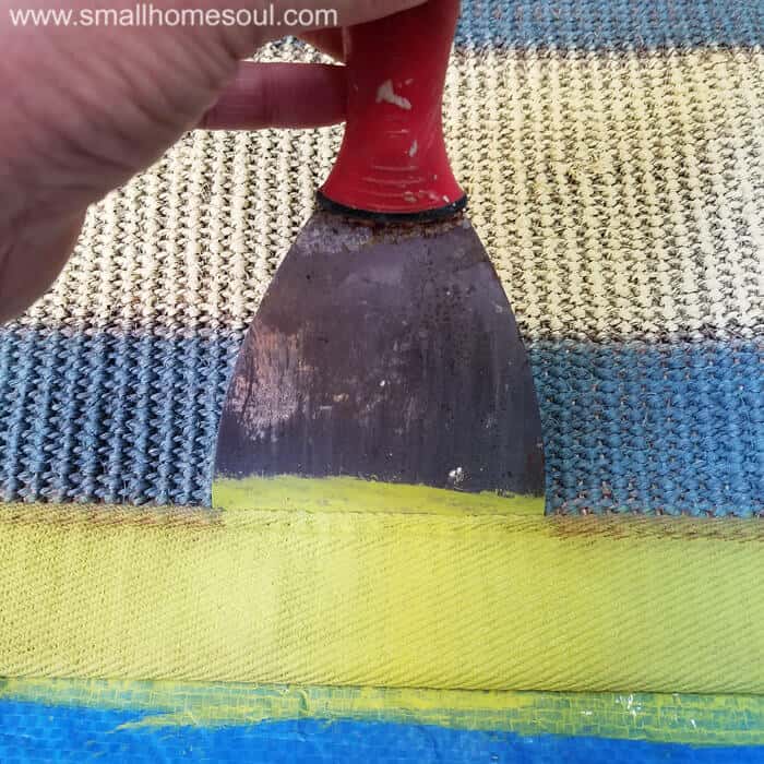 A putty knife helps paint a rug border.