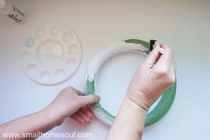 Painting a green form wreath form with white craft paint.