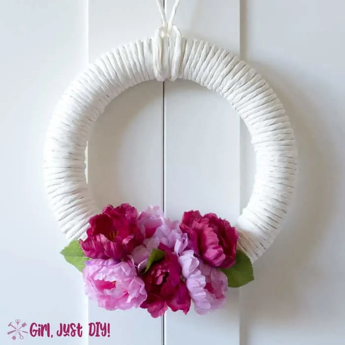 light and dark pink flowers on white wreath hanging from white door.
