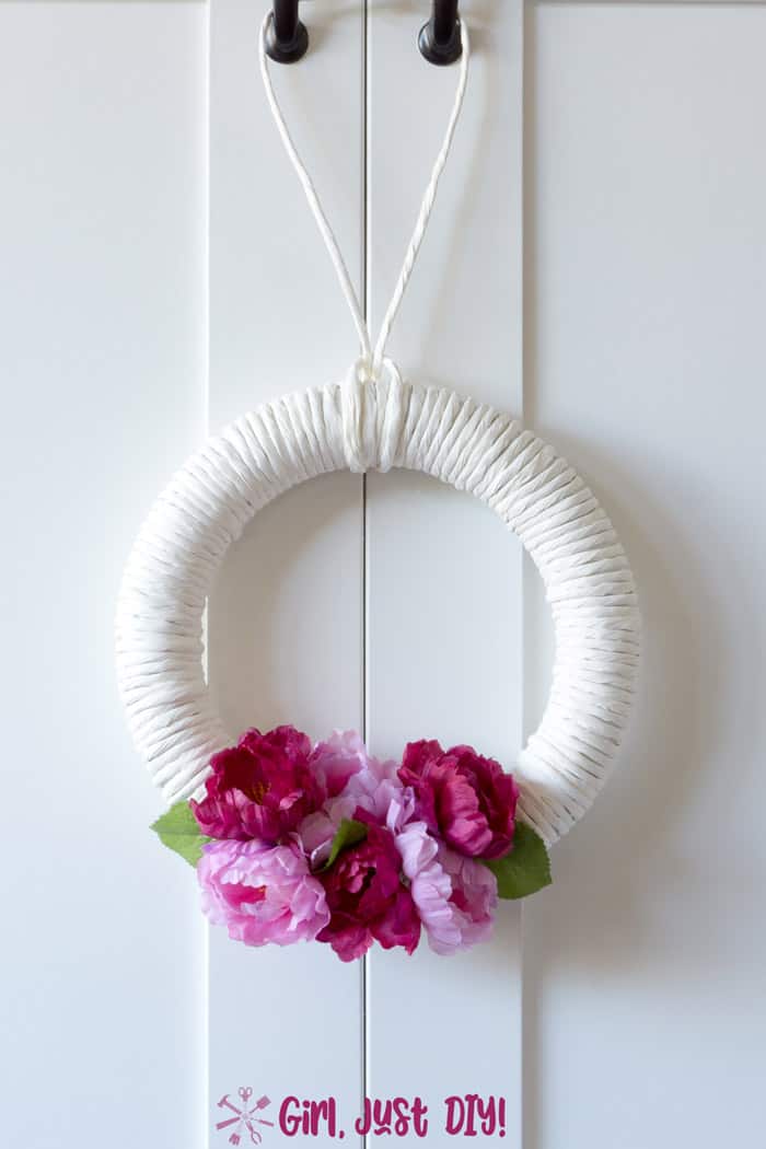 white wreath with dark and light pink flowers hanging on white door.