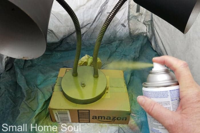 Applying green spray paint for desk lamp makeover.