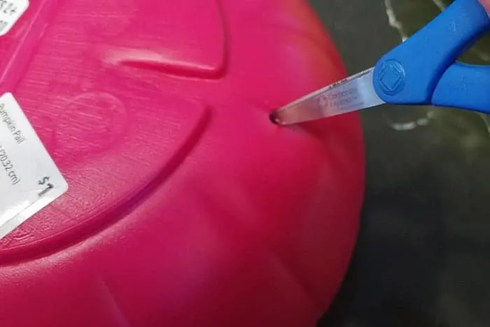 Cutting hole in bottom of plastic pumpkin to make it a light up pumpkin.