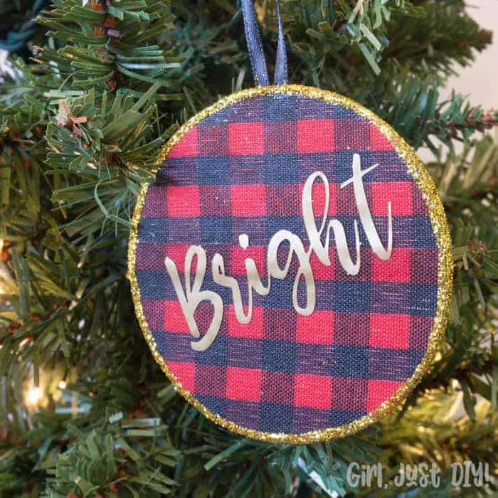 Buffalo plaid christmas ornament with gold glitter trim on lighted tree.