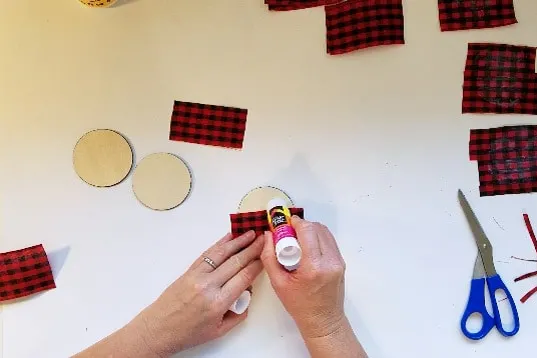 Putting glue stick onto buffalo plaid Christmas ornament round.