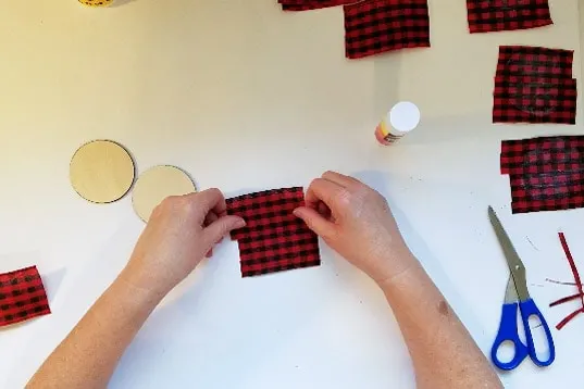 Placing ribbon fabric on buffalo plaid christmas ornament round.