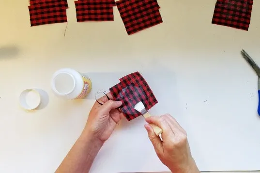 Painting Mod Podge onto fabric of buffalo plaid on ornament.