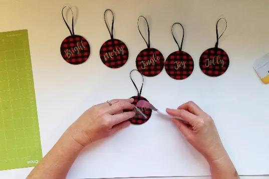 Affixing cricut vinyl word to buffalo plaid ornaments.