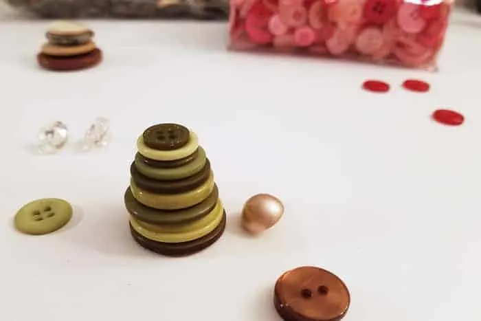 Stacked green buttons on table making button christmas ornaments.