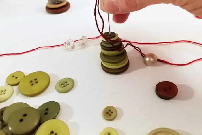 Needle threaded through stacked green buttons for button christmas trees.