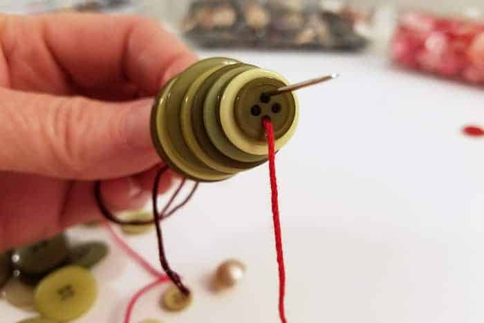 Returning needle through other side of green buttons for button christmas ornaments.