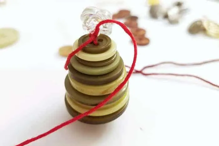 Tying a clear button to top of button Christmas tree ornaments.