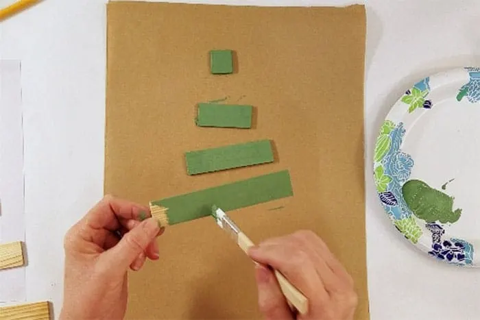 Paint sticks being painted green for christmas tree craft.