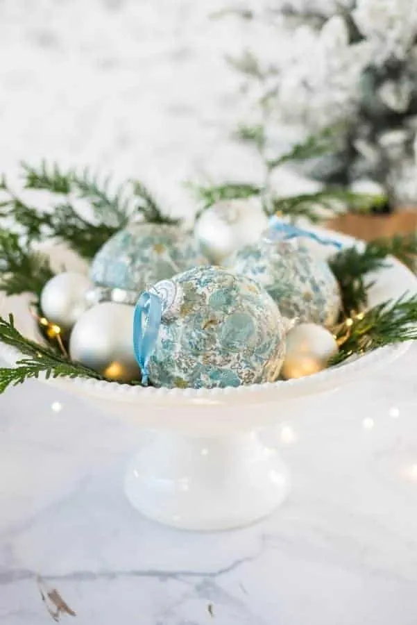 Decoupage DIY Christmas Ornaments in blue and white in a bowl with greenery.