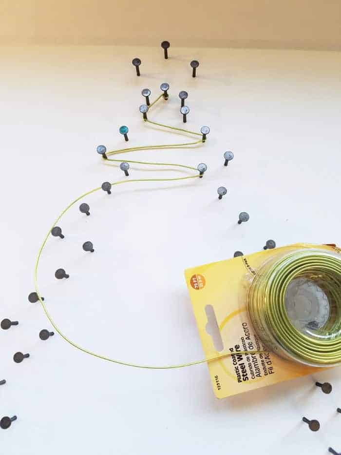 Wrapping green wire on every other nail on Christmas tree string art.