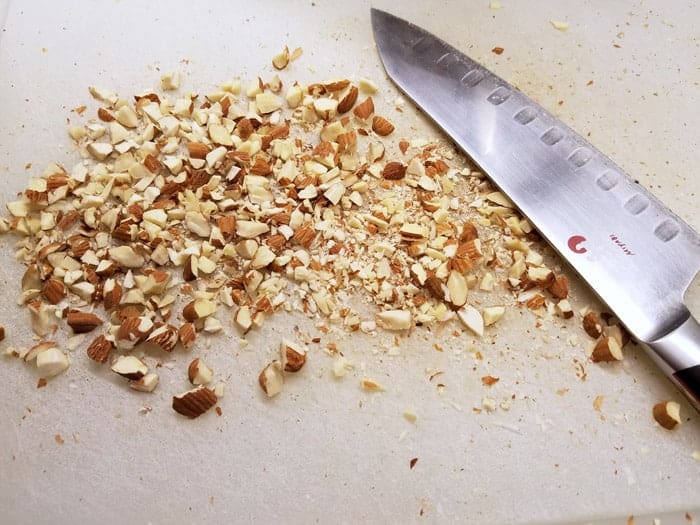 Chopped almonds on cutting board with chef's knife.