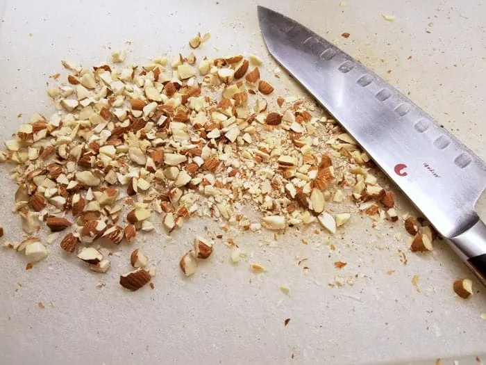 Chopped almonds on cutting board with chef's knife.