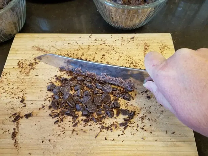 Chopping chocolate chips with chef's knife on cutting board.